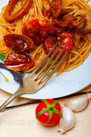 Italian seafood spaghetti pasta on red tomato sauce over white rustic wood table