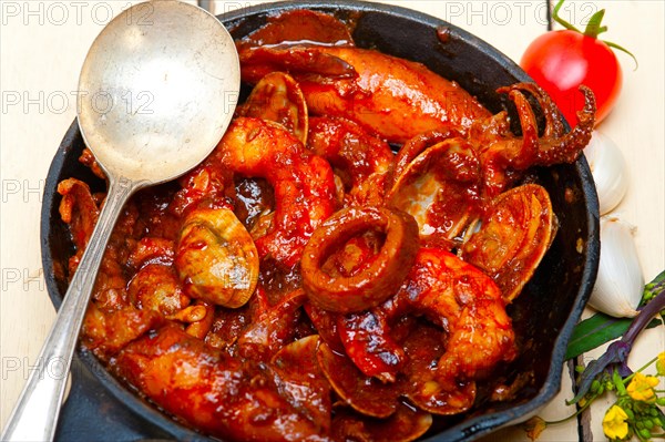 Fresh seafood stew prepared on an iron skillet ove white rustic wood table