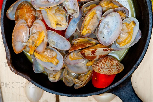 Fresh clams stewed on an iron skillet over wite rustic wood table