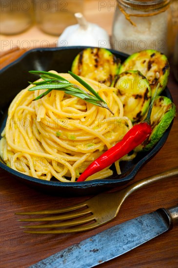 Italian spaghetti pasta with zucchini sauce on iron skillet over wood board