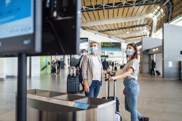 Two travelling women wearing protective masks discussing by flight information board at the Faro airport