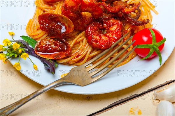 Italian seafood spaghetti pasta on red tomato sauce over white rustic wood table