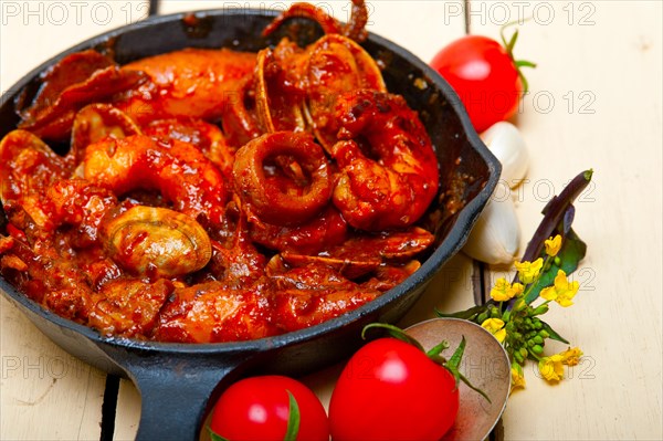 Fresh seafood stew prepared on an iron skillet ove white rustic wood table