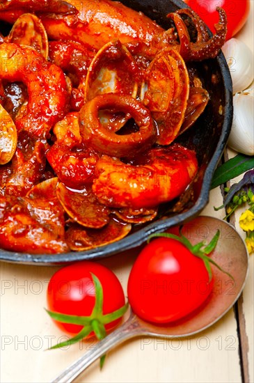 Fresh seafood stew prepared on an iron skillet ove white rustic wood table