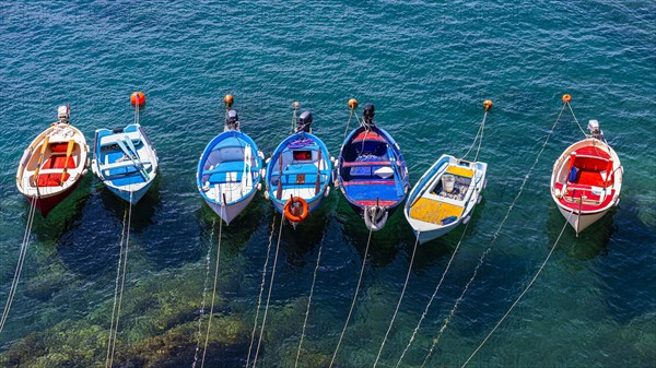 Colourful fishing boats attached to the rock lie in the turquoise water in the harbour of Riomaggiore