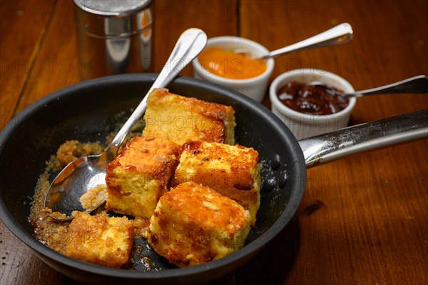 Brown caramelised Kaiserschmarren in a cast iron pan for dessert and two small bowls with jam and a sprinkling for icing sugar