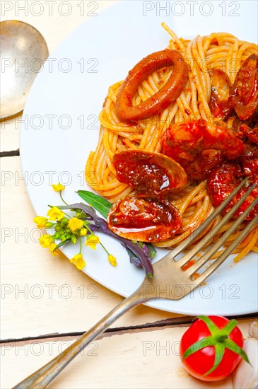 Italian seafood spaghetti pasta on red tomato sauce over white rustic wood table