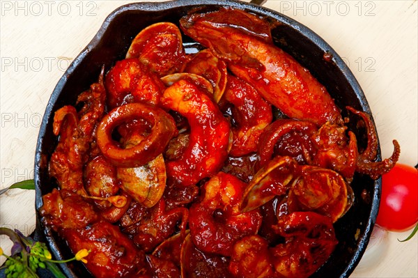 Fresh seafood stew prepared on an iron skillet ove white rustic wood table