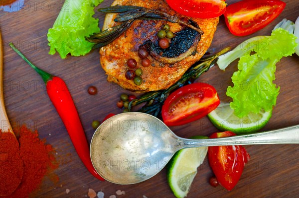 Wood fired hoven cooked chicken breast on wood board with herbs spices and vegetables