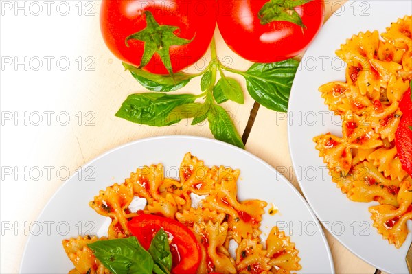 Italian pasta farfalle butterfly bow-tie with tomato basil sauce over white rustic wood table