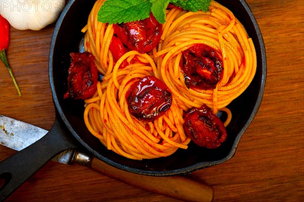 Italian spaghetti pasta and tomato with mint leaves on iron skillet over wood board