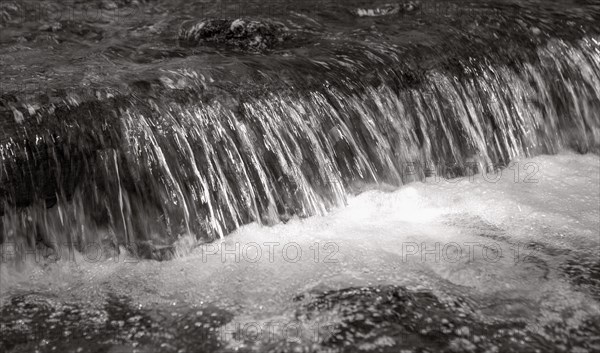 Flowing water with small waterfall and light reflections