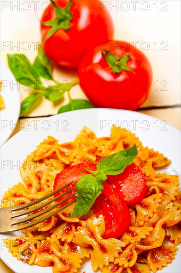 Italian pasta farfalle butterfly bow-tie with tomato basil sauce over white rustic wood table