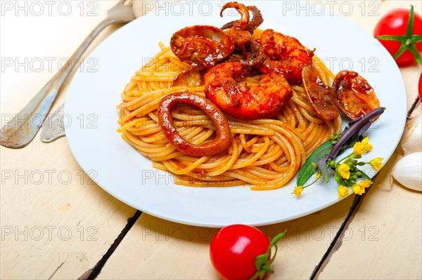 Italian seafood spaghetti pasta on red tomato sauce over white rustic wood table