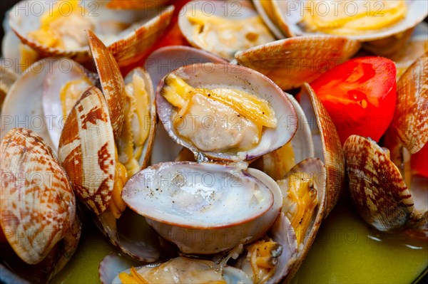 Fresh clams stewed on an iron skillet over wite rustic wood table