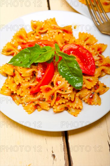 Italian pasta farfalle butterfly bow-tie with tomato basil sauce over white rustic wood table