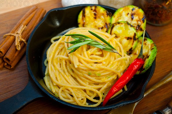 Italian spaghetti pasta with zucchini sauce on iron skillet over wood board