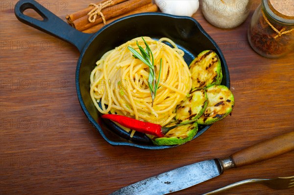 Italian spaghetti pasta with zucchini sauce on iron skillet over wood board