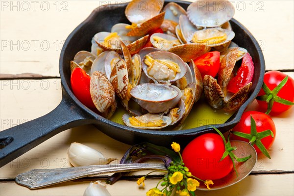 Fresh clams stewed on an iron skillet over wite rustic wood table