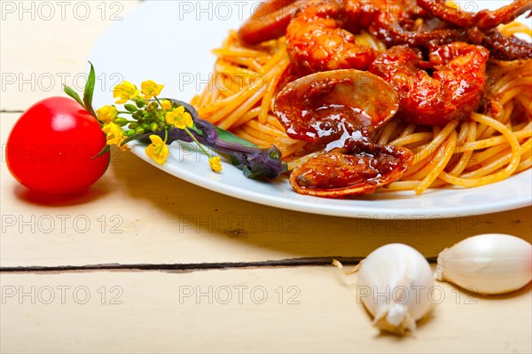 Italian seafood spaghetti pasta on red tomato sauce over white rustic wood table