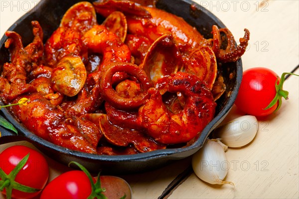 Fresh seafood stew prepared on an iron skillet ove white rustic wood table