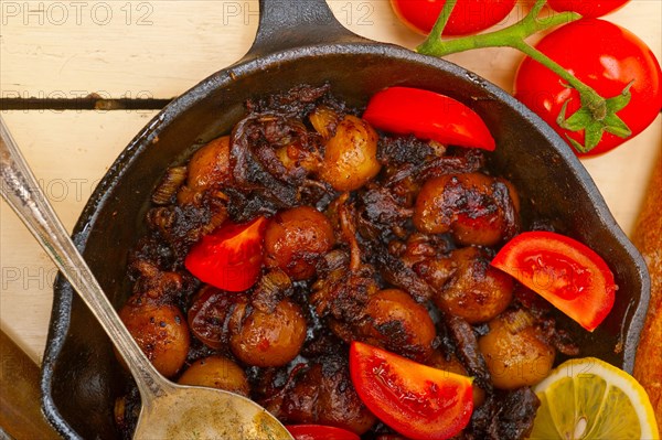 Baby cuttle fish roasted on iron skillet with tomatoes and onions over rustic wood table