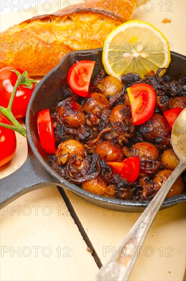 Baby cuttle fish roasted on iron skillet with tomatoes and onions over rustic wood table