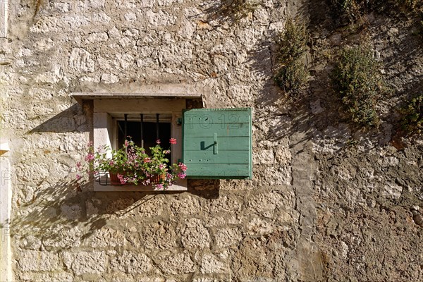 Small window with wooden beams and flowerpot of a stone-built house in the warm evening light