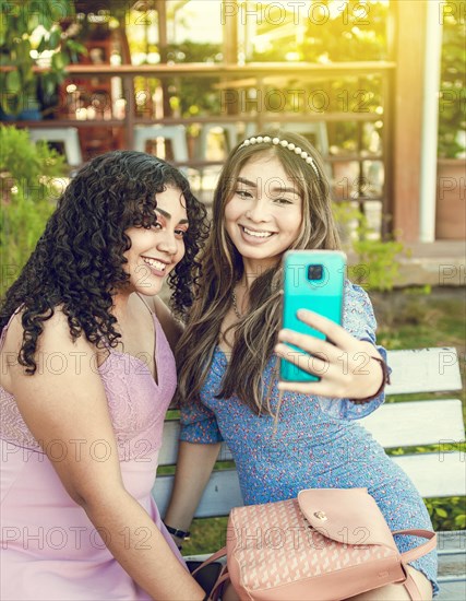 Two pretty girls sitting on a bench taking a selfie