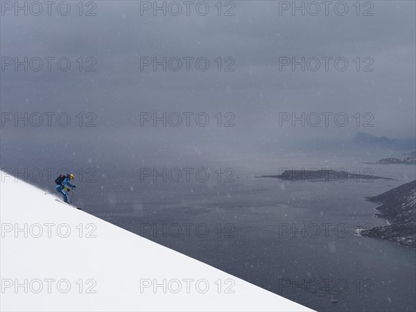 Skiers in light snowfall in front of the sea