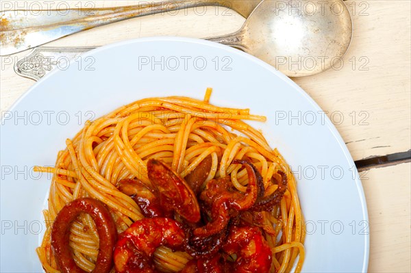 Italian seafood spaghetti pasta on red tomato sauce over white rustic wood table