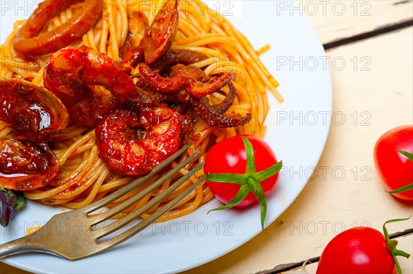 Italian seafood spaghetti pasta on red tomato sauce over white rustic wood table