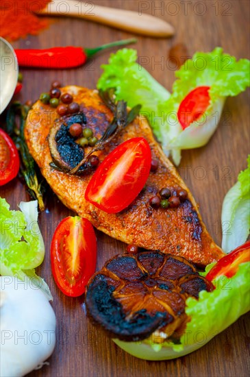 Wood fired hoven cooked chicken breast on wood board with herbs spices and vegetables