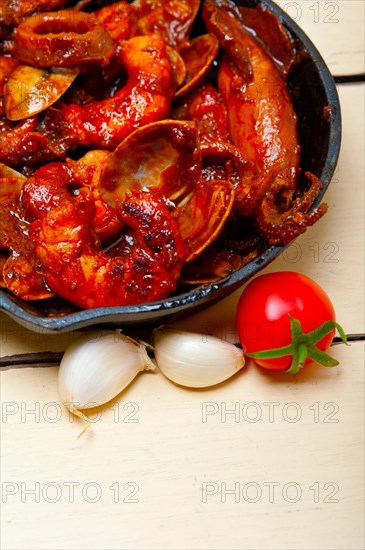 Fresh seafood stew prepared on an iron skillet ove white rustic wood table