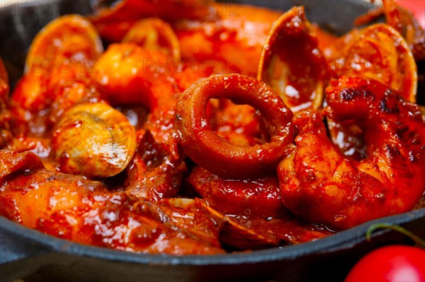 Fresh seafood stew prepared on an iron skillet ove white rustic wood table