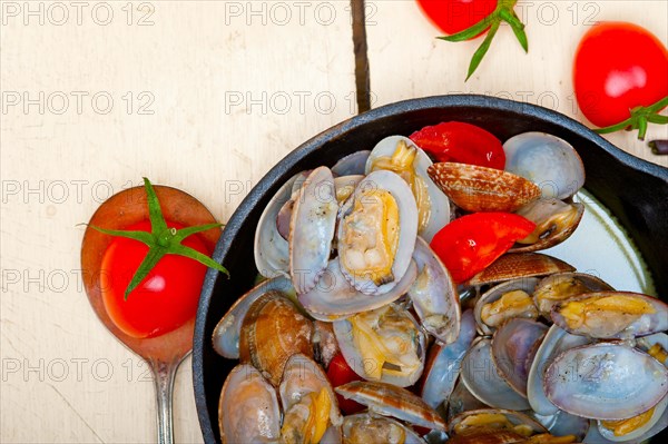 Fresh clams stewed on an iron skillet over wite rustic wood table