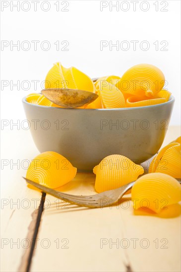 Raw Italian snail lumaconi pasta on a blue bowl over rustic table macro