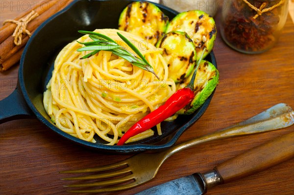 Italian spaghetti pasta with zucchini sauce on iron skillet over wood board