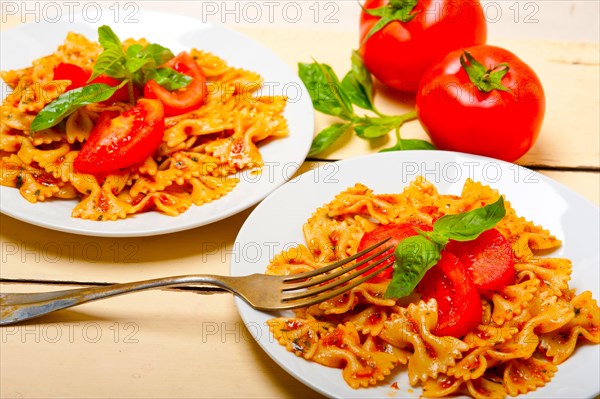 Italian pasta farfalle butterfly bow-tie with tomato basil sauce over white rustic wood table