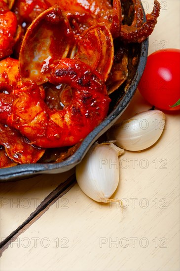 Fresh seafood stew prepared on an iron skillet ove white rustic wood table