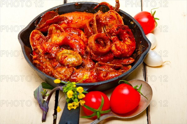 Fresh seafood stew prepared on an iron skillet ove white rustic wood table