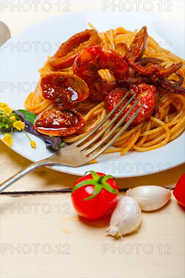 Italian seafood spaghetti pasta on red tomato sauce over white rustic wood table