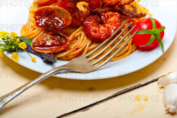 Italian seafood spaghetti pasta on red tomato sauce over white rustic wood table