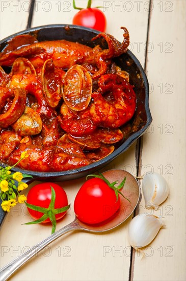 Fresh seafood stew prepared on an iron skillet ove white rustic wood table