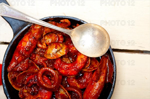 Fresh seafood stew prepared on an iron skillet ove white rustic wood table