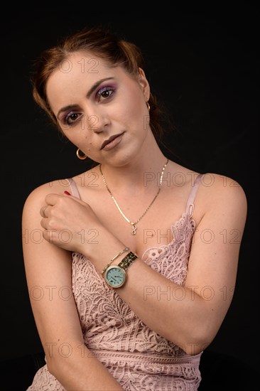 Pretty young woman with made-up eyes in sleeveless pink dress against black background