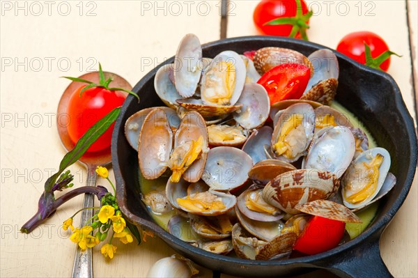 Fresh clams stewed on an iron skillet over wite rustic wood table