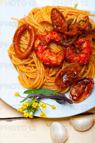 Italian seafood spaghetti pasta on red tomato sauce over white rustic wood table