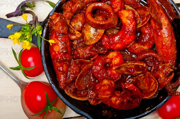 Fresh seafood stew prepared on an iron skillet ove white rustic wood table