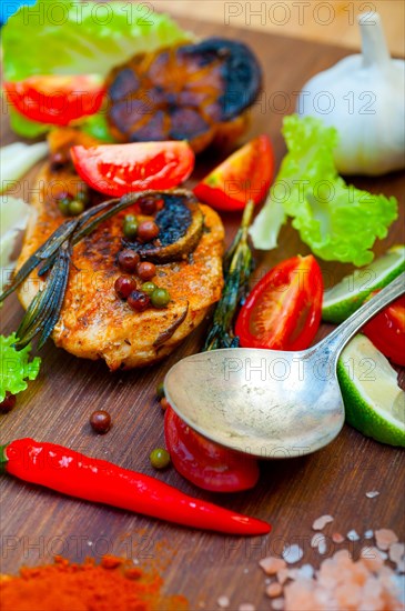 Wood fired hoven cooked chicken breast on wood board with herbs spices and vegetables